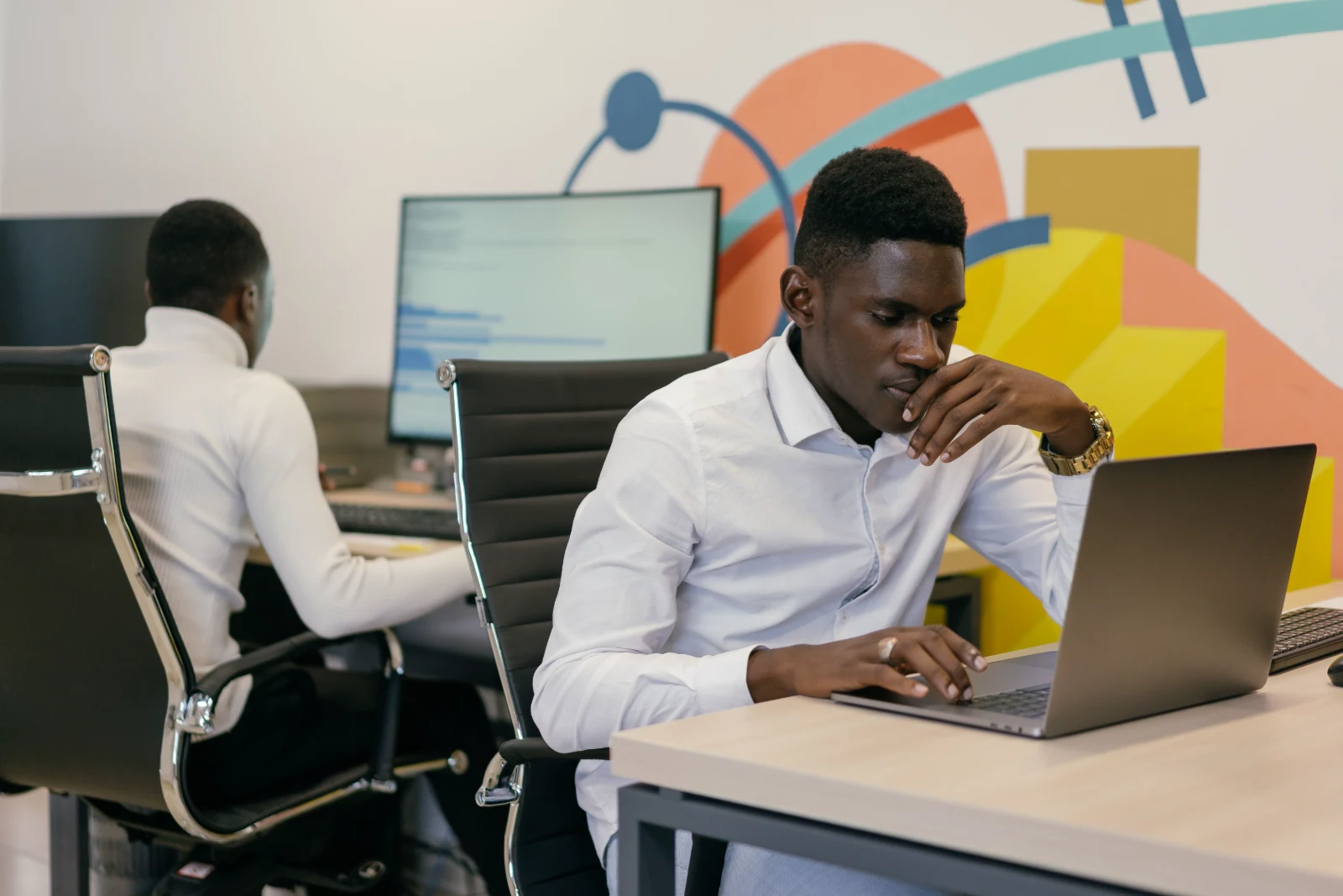 Two colleagues working at laptops in a bright studio with a painted feature wall