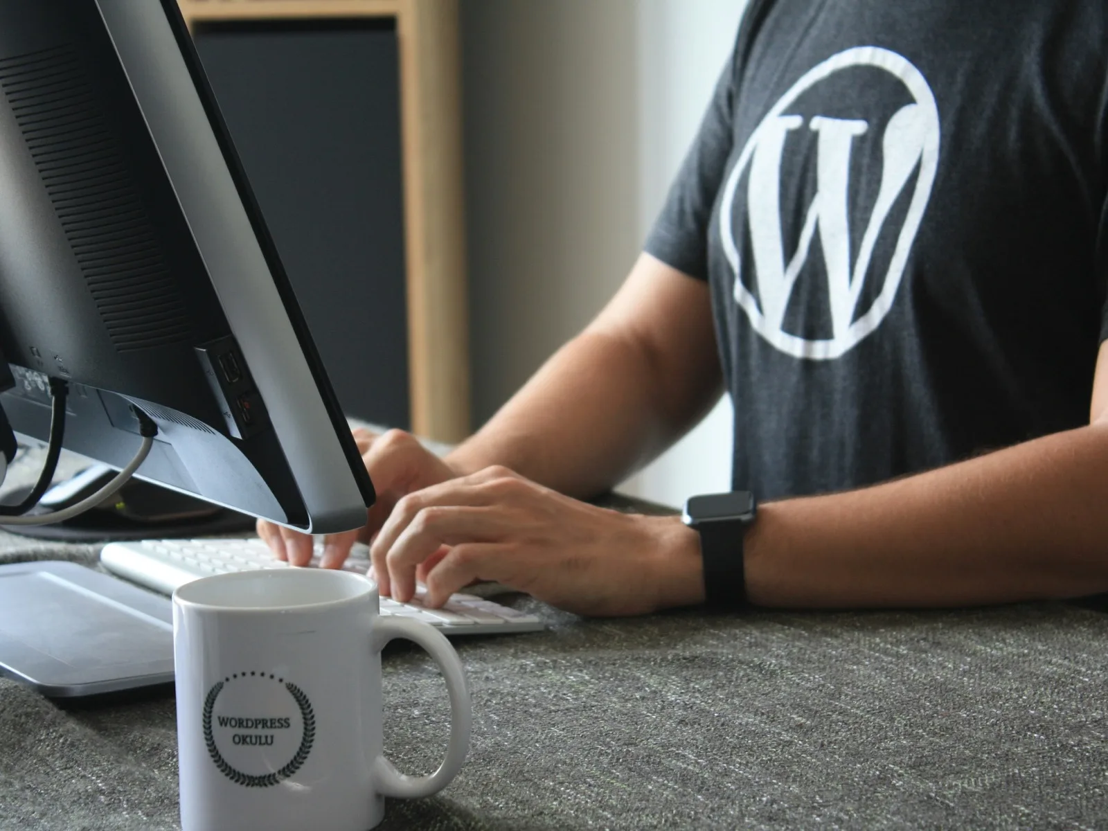 A person working at a desktop computer wearing a WordPress logo shirt