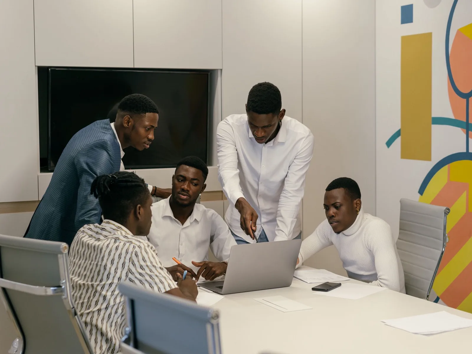 A group gathered around a laptop in a modern office with a painted feature wall